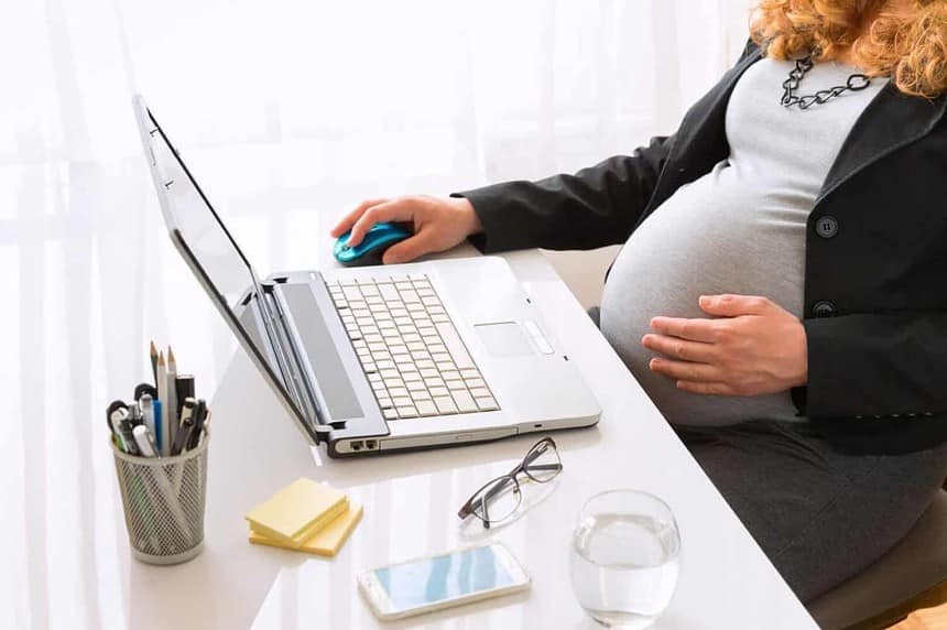 Pregnant woman working at office desk with laptop.