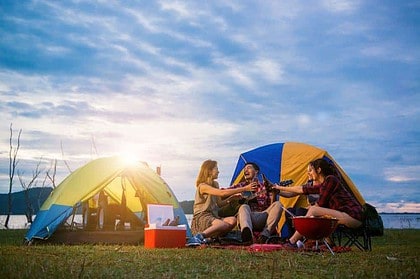 Friends toasting at a lakeside camping trip during sunset.