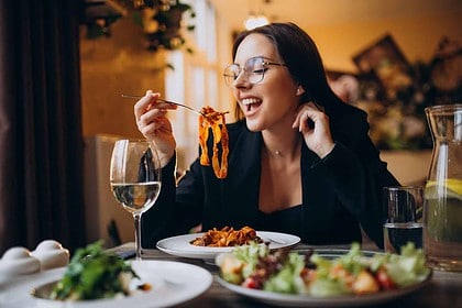 Happy woman eating pasta in a cozy restaurant setting.