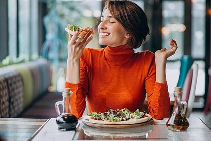 Woman savoring pizza slice at a cozy pizzeria.