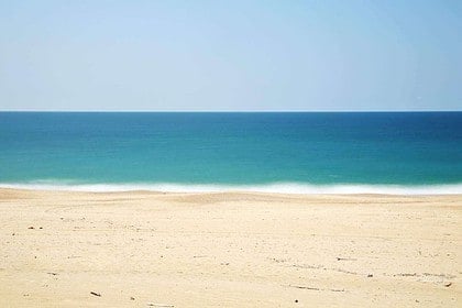 Tranquil sandy beach with clear blue sea under sunny sky.