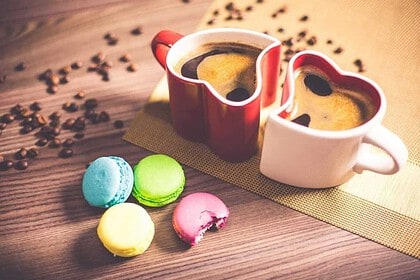 Two cups of coffee with colorful macarons on a wooden table.
