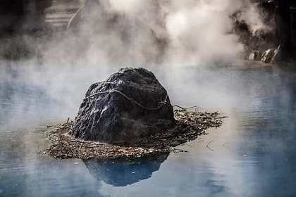Misty hot springs with rocky outcrop in serene setting.