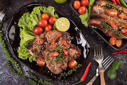 Herb-crusted sesame pork steak with tomatoes and lime.