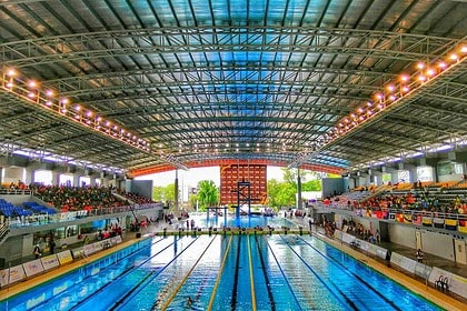 Large indoor swimming pool with spectator stands and bright lighting.