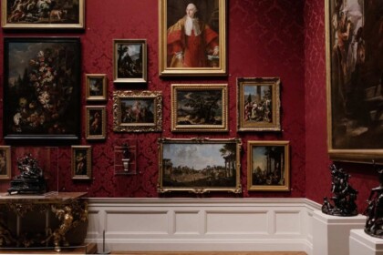 Diverse paintings on red wall in art gallery exhibit.