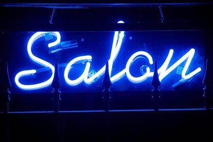 Illuminated neon salon sign at night.
