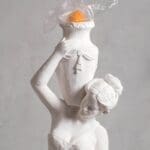 Statue with orange headpiece and plastic-wrap effect.