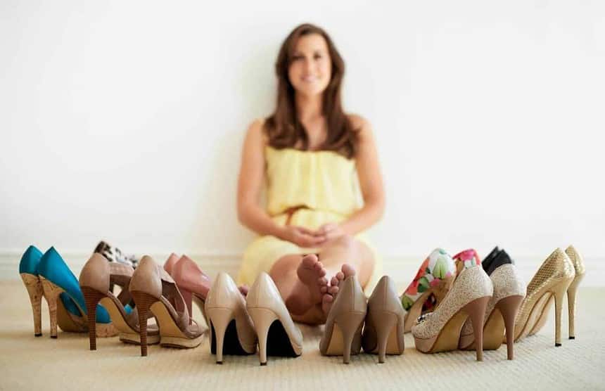 Young woman with a diverse shoe collection displayed around her.