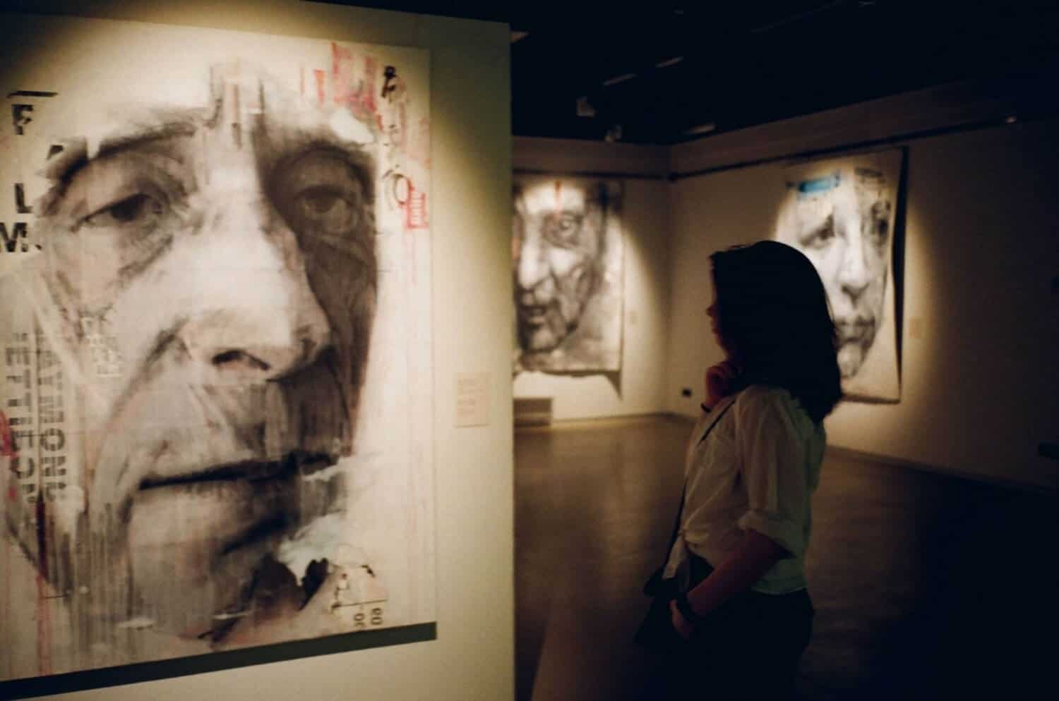 Person viewing expressive portraits at art gallery exhibit.