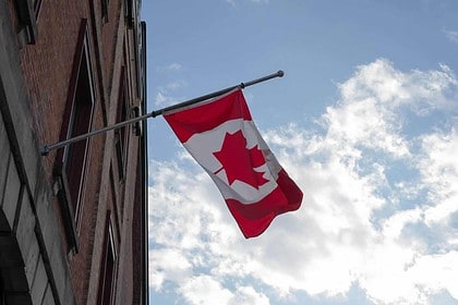 Canadian flag waving on building exterior against sky.