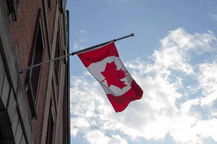 Canadian flag waving on building exterior against sky.
