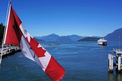 Canadian flag over ferry crossing scenic mountainous coastline.