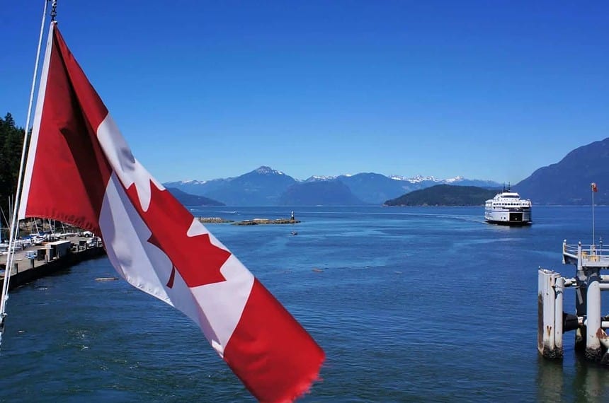 Canadian flag over ferry crossing scenic mountainous coastline.