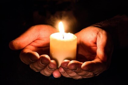 Cupped hands holding a lit candle in darkness.