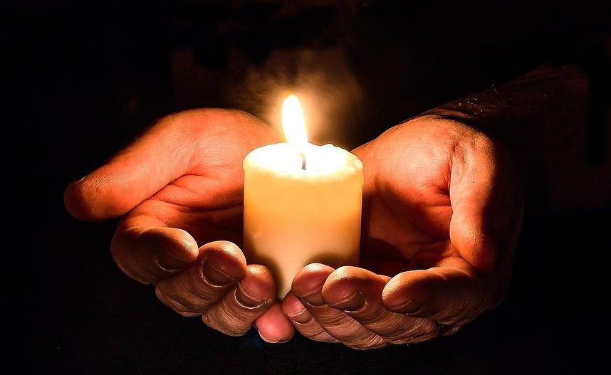 Cupped hands holding a lit candle in darkness.