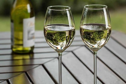 Two glasses of white wine on an outdoor table.