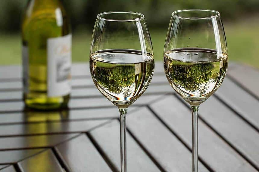 Two glasses of white wine on an outdoor table.
