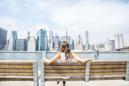 Woman sitting on bench enjoying Manhattan skyline view.