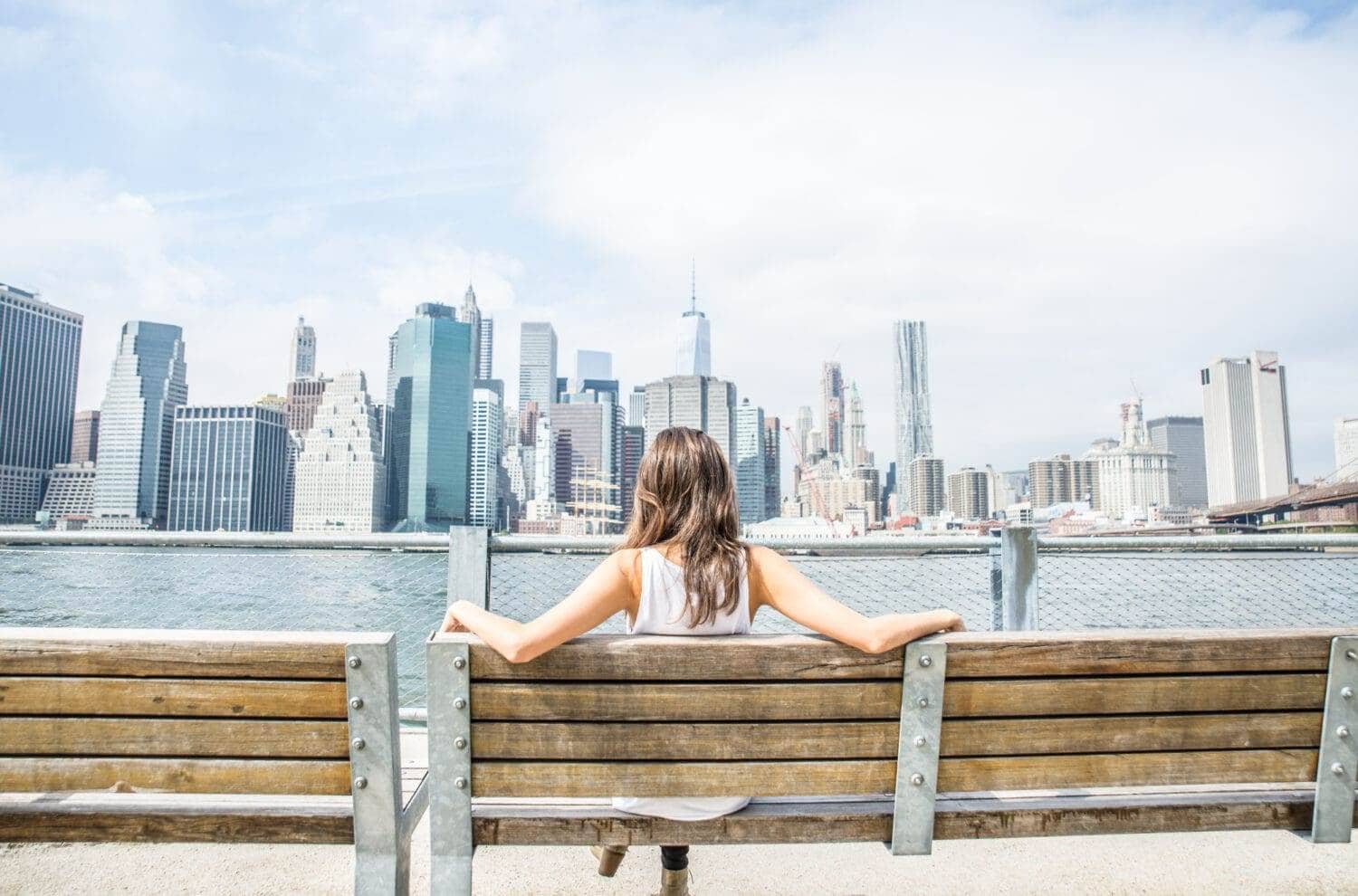 Woman sitting on bench enjoying Manhattan skyline view.