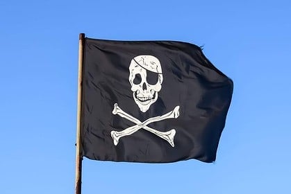 Black pirate flag with skull and crossbones waving against blue sky.