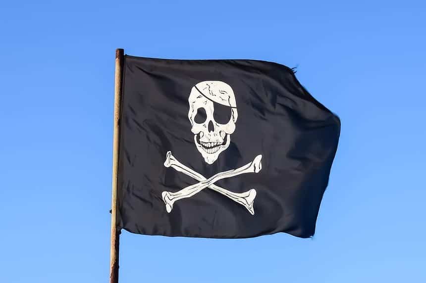 Black pirate flag with skull and crossbones waving against blue sky.