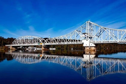Scenic blue bridge with clear reflection on calm water against sky.