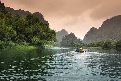 Serene dusk scene with boat on tranquil lake surrounded by mountains.