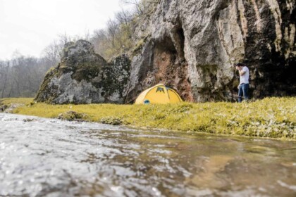 Tent by riverside with cliff backdrop in natural setting.