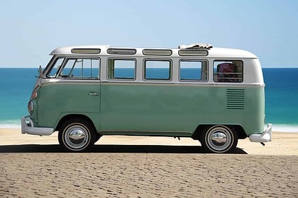 Vintage minivan parked on beach with ocean backdrop.