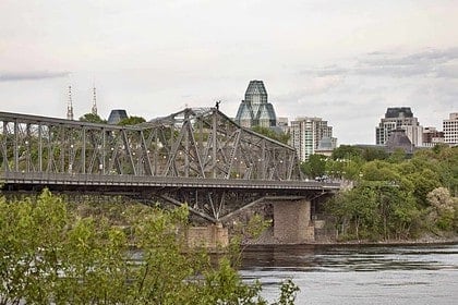 Scenic view of a truss bridge crossing the Ottawa River with city skyline.