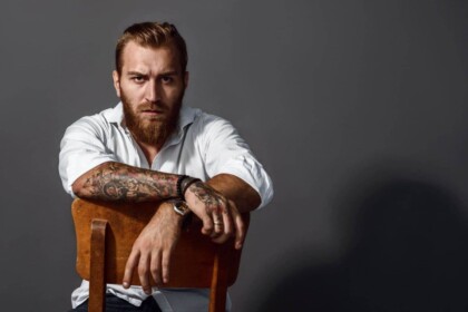 Handsome man with tattoos wearing white shirt sitting on a chair.