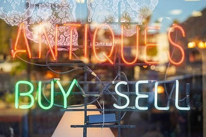 Neon sign of antiques shop offering buying and selling services.