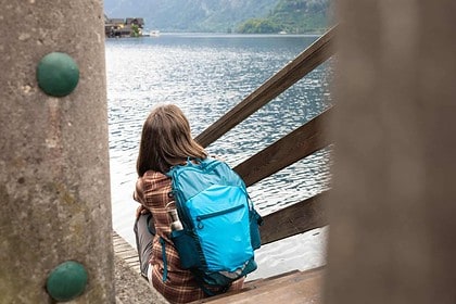 Woman sitting on steps with backpack enjoying lakeside view.