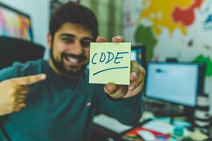 Man pointing at sticky note with CODE in office setting.
