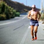 Man jogging on a sunny road in athletic shorts and running shoes.