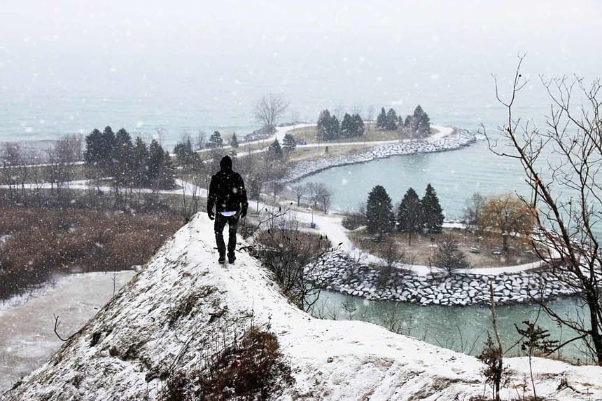 Person overlooking snowy Scarborough Bluffs in winter.