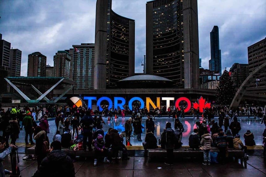 Twilight at Toronto City Hall with illuminated sign and crowd.