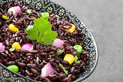 Black rice with colorful vegetables in decorative bowl.