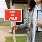Real estate agent holding Home For Sale sign.
