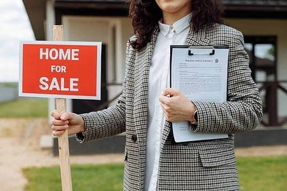 Real estate agent holding Home For Sale sign.