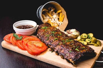 Juicy oven-baked beef ribs with garnishes on a wooden board.