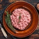 Raw ground turkey with herbs on dark wood surface.