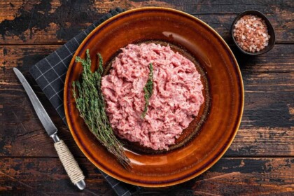 Raw ground turkey with herbs on dark wood surface.