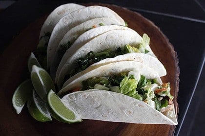Row of fresh tacos with lime on dark background.