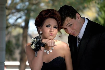 Teen couple dressed up for prom, posing outdoors.