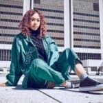 Woman in green urban outfit sitting on pavement.