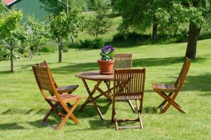 Outdoor wooden furniture set on grass with potted plant.
