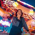 Woman smiling at camera with amusement park rides at night.