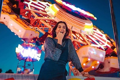 Woman smiling at camera with amusement park rides at night.